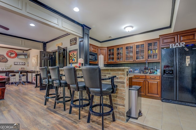 kitchen featuring a kitchen breakfast bar, backsplash, crown molding, black appliances, and light wood-type flooring