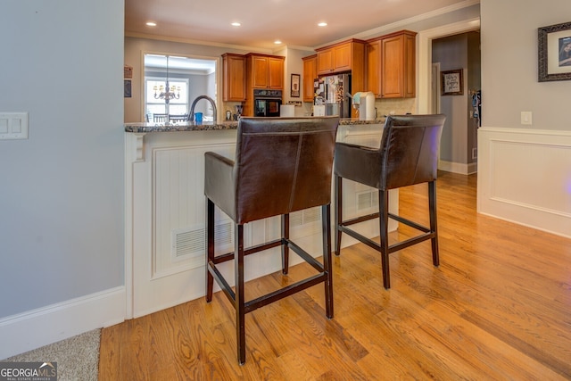 kitchen featuring oven, light wood-type flooring, kitchen peninsula, a breakfast bar area, and stainless steel refrigerator