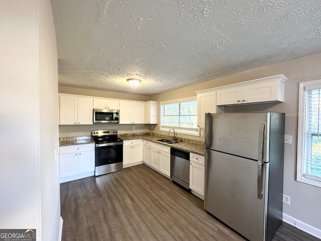 kitchen with appliances with stainless steel finishes, dark hardwood / wood-style flooring, white cabinetry, and sink