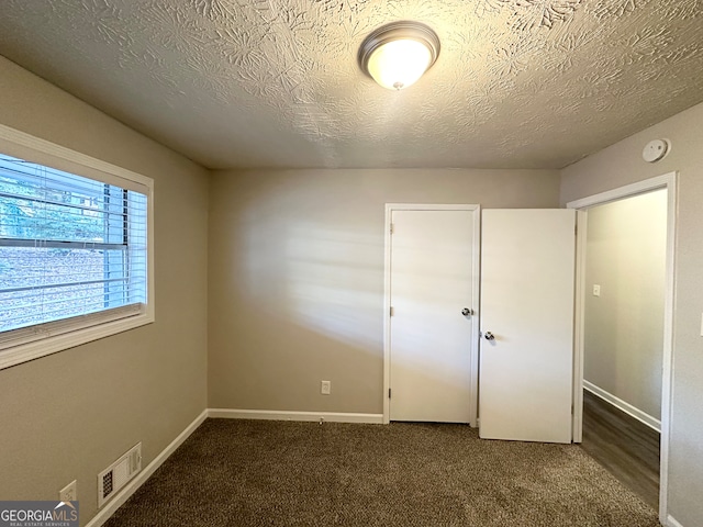 unfurnished bedroom featuring dark carpet and a textured ceiling