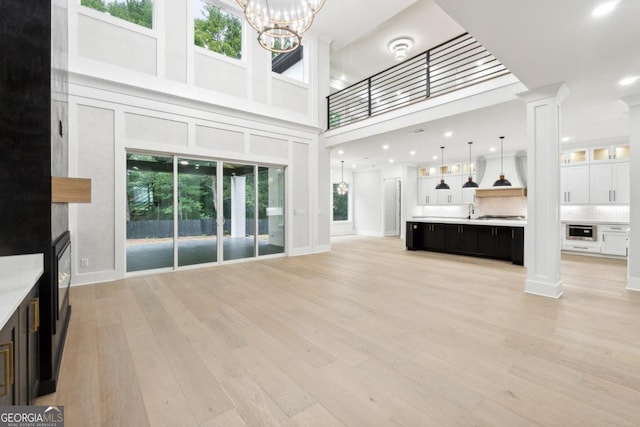 unfurnished living room with decorative columns, a towering ceiling, and light hardwood / wood-style flooring