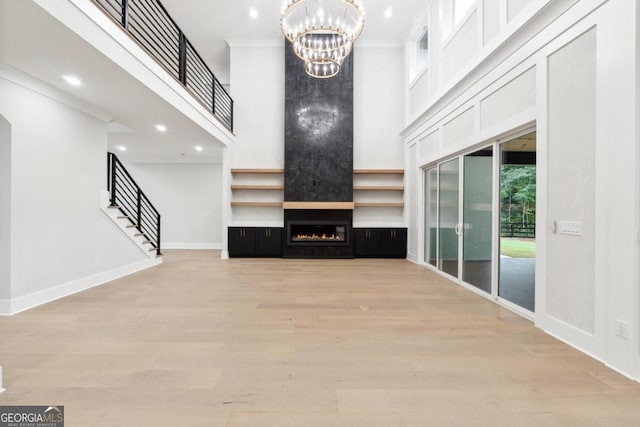 unfurnished living room with a large fireplace, a towering ceiling, light hardwood / wood-style floors, and ornamental molding