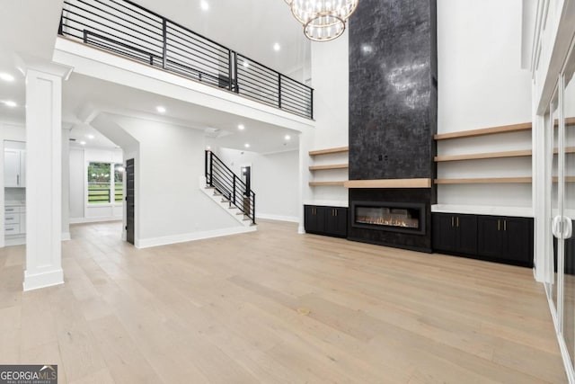 unfurnished living room featuring a large fireplace, light hardwood / wood-style floors, a towering ceiling, and a chandelier