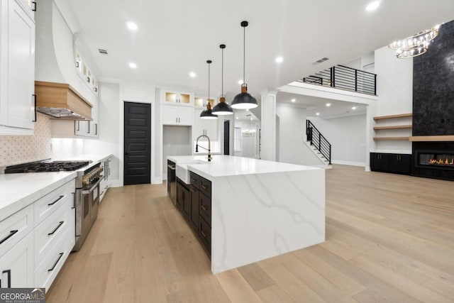 kitchen with high end range, a spacious island, sink, custom range hood, and white cabinetry