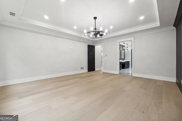 interior space with an inviting chandelier, a tray ceiling, light hardwood / wood-style flooring, and ornamental molding