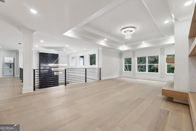 unfurnished living room with light wood-type flooring, an inviting chandelier, a raised ceiling, and crown molding