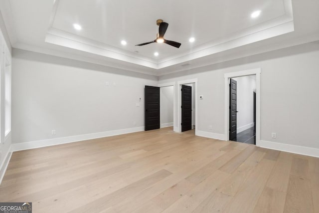 unfurnished bedroom featuring ceiling fan, light hardwood / wood-style floors, a raised ceiling, and a walk in closet