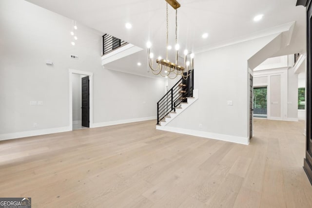 unfurnished living room featuring a high ceiling, an inviting chandelier, and light hardwood / wood-style flooring