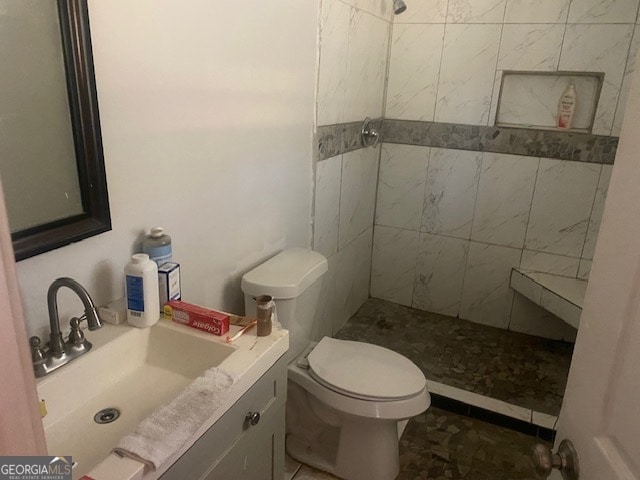 bathroom featuring tiled shower, vanity, toilet, and tile patterned flooring