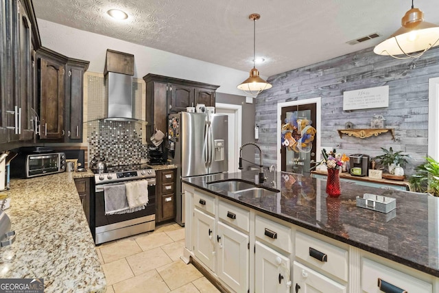 kitchen with dark brown cabinetry, sink, wall chimney exhaust hood, wood walls, and appliances with stainless steel finishes