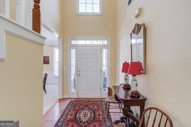 entrance foyer featuring a healthy amount of sunlight, a towering ceiling, visible vents, and wood finished floors