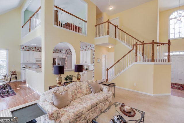 living area with baseboards, arched walkways, a towering ceiling, light wood-style flooring, and stairway