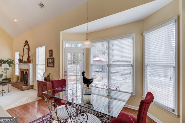 dining area featuring baseboards, visible vents, wood finished floors, vaulted ceiling, and a brick fireplace