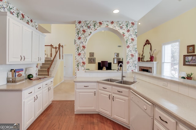 kitchen featuring white dishwasher, a sink, white cabinets, light wood-style floors, and light countertops