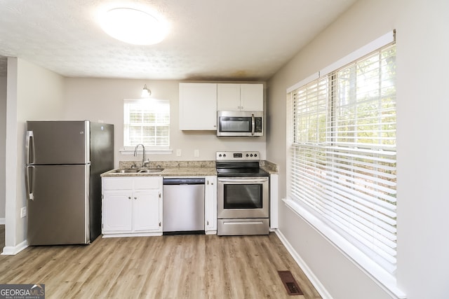 kitchen featuring appliances with stainless steel finishes, a textured ceiling, sink, light hardwood / wood-style flooring, and white cabinetry