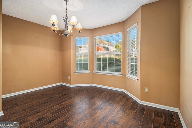 empty room featuring a textured ceiling, dark wood-type flooring, and an inviting chandelier