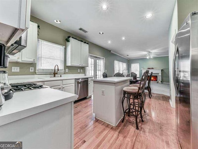 kitchen with white cabinetry, light hardwood / wood-style floors, a kitchen bar, a kitchen island, and appliances with stainless steel finishes