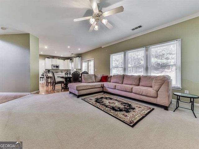 living room featuring ceiling fan, crown molding, and light colored carpet