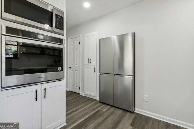 kitchen featuring white cabinets, appliances with stainless steel finishes, a textured ceiling, and dark wood-type flooring