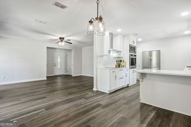 kitchen with stainless steel appliances, wall chimney range hood, dark hardwood / wood-style flooring, decorative light fixtures, and white cabinets