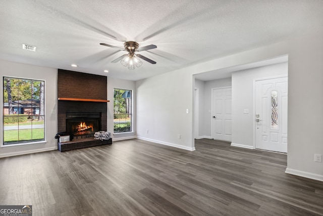 unfurnished living room with ceiling fan, dark wood-type flooring, a textured ceiling, and a brick fireplace