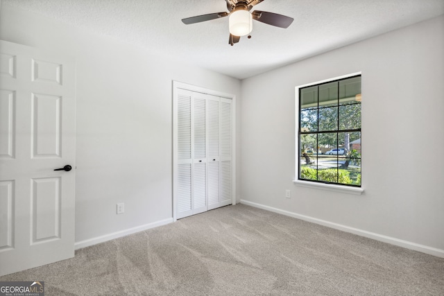 unfurnished bedroom featuring light carpet, a textured ceiling, a closet, and ceiling fan