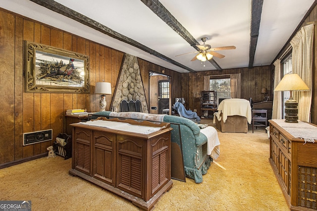 carpeted bedroom with ceiling fan, beam ceiling, a stone fireplace, and wooden walls