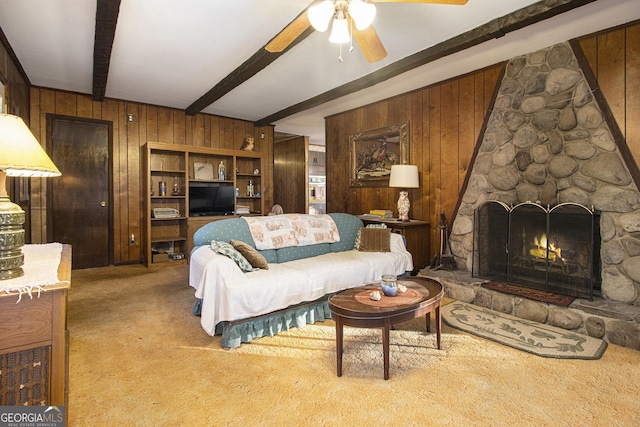 living room featuring wood walls, ceiling fan, a fireplace, beamed ceiling, and light colored carpet