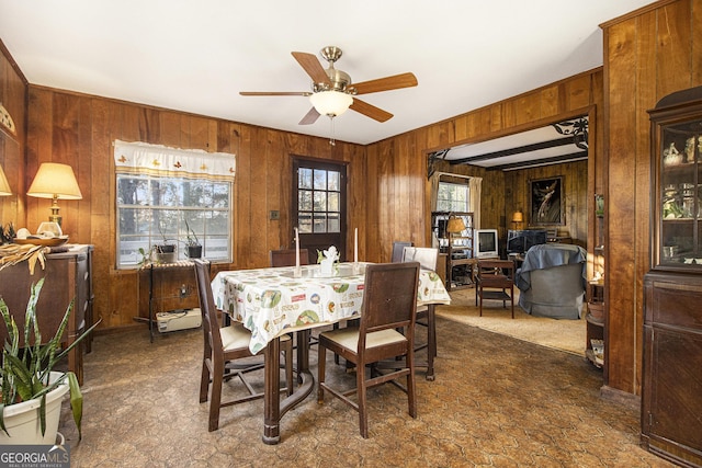 carpeted dining room with wood walls and ceiling fan