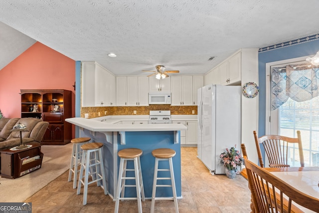 kitchen with a breakfast bar, a textured ceiling, white appliances, vaulted ceiling, and white cabinetry