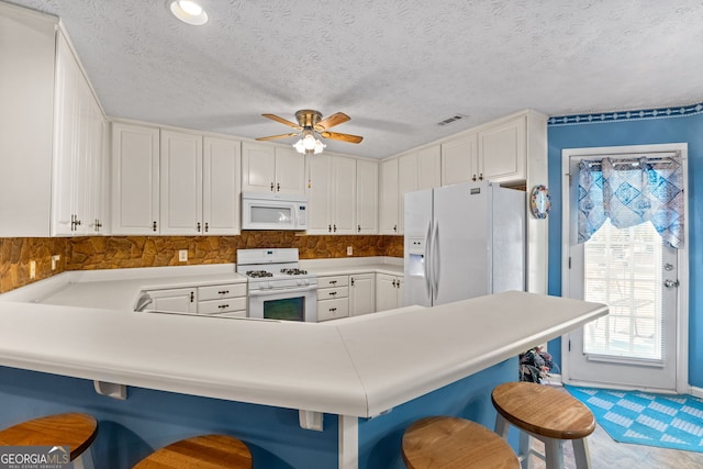 kitchen with kitchen peninsula, a kitchen breakfast bar, white appliances, ceiling fan, and white cabinetry