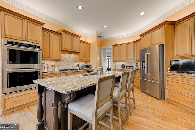 kitchen with light stone counters, an island with sink, decorative backsplash, a breakfast bar, and appliances with stainless steel finishes