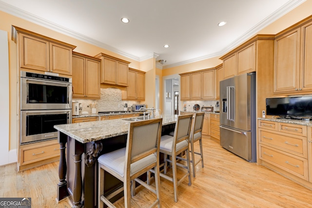 kitchen featuring light stone counters, backsplash, an island with sink, a breakfast bar area, and appliances with stainless steel finishes