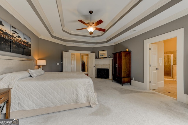 bedroom featuring ensuite bath, ceiling fan, a tray ceiling, a tiled fireplace, and ornamental molding