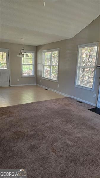 carpeted empty room with a healthy amount of sunlight, an inviting chandelier, and vaulted ceiling