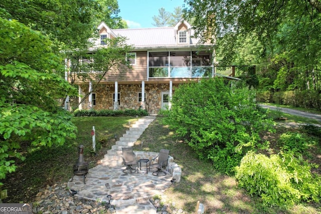 exterior space with stone siding, a sunroom, metal roof, and stairway