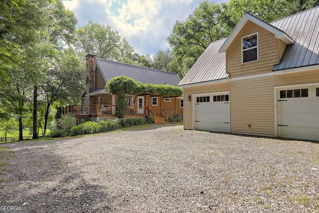 view of front of home featuring a chimney, a standing seam roof, metal roof, a garage, and driveway