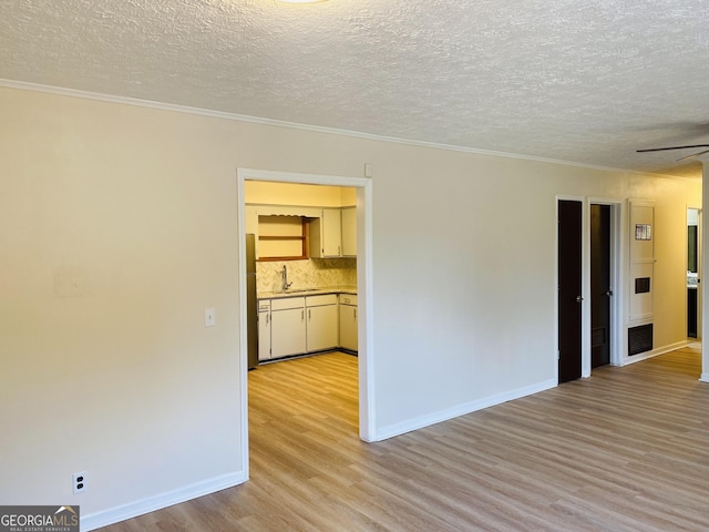 empty room featuring sink, crown molding, ceiling fan, light wood-type flooring, and a textured ceiling