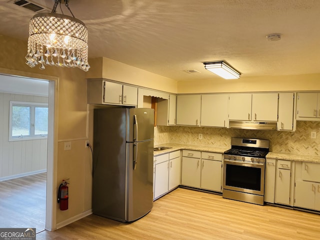 kitchen featuring light wood-type flooring, tasteful backsplash, stainless steel appliances, pendant lighting, and a chandelier