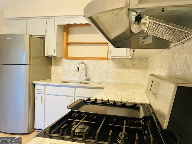 kitchen with stainless steel refrigerator, white cabinetry, sink, extractor fan, and light hardwood / wood-style floors