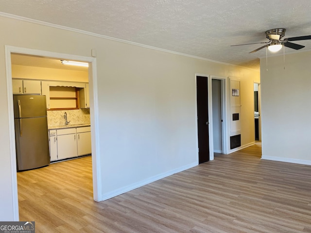 unfurnished room with light wood-type flooring, a textured ceiling, ceiling fan, crown molding, and sink