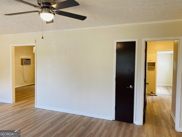 spare room with ornamental molding, a textured ceiling, a wall unit AC, ceiling fan, and light hardwood / wood-style flooring