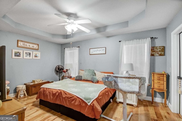 bedroom with ceiling fan, light hardwood / wood-style floors, multiple windows, and a tray ceiling