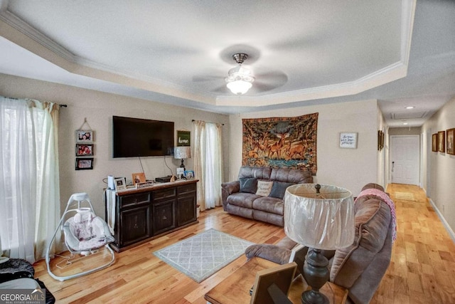 living room with a tray ceiling, ceiling fan, ornamental molding, and light wood-type flooring