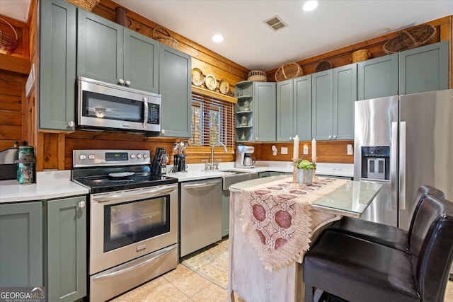 kitchen with appliances with stainless steel finishes, light tile patterned floors, wood walls, and sink