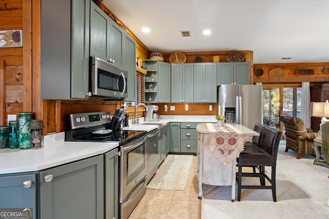 kitchen with wood walls, sink, light tile patterned floors, a kitchen bar, and stainless steel appliances