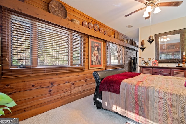 carpeted bedroom featuring a stone fireplace, wooden walls, and ceiling fan