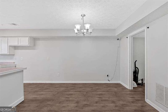 unfurnished dining area with a textured ceiling, dark wood-type flooring, and a notable chandelier