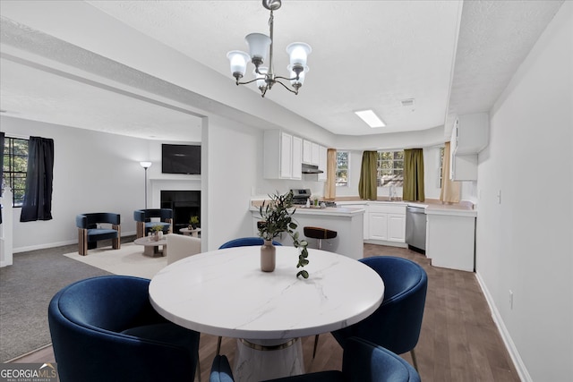 dining area featuring a tile fireplace, a healthy amount of sunlight, dark hardwood / wood-style floors, and a notable chandelier