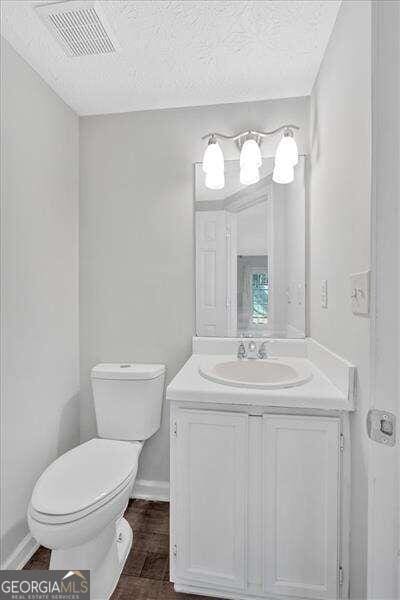 bathroom with hardwood / wood-style floors, vanity, toilet, and a textured ceiling